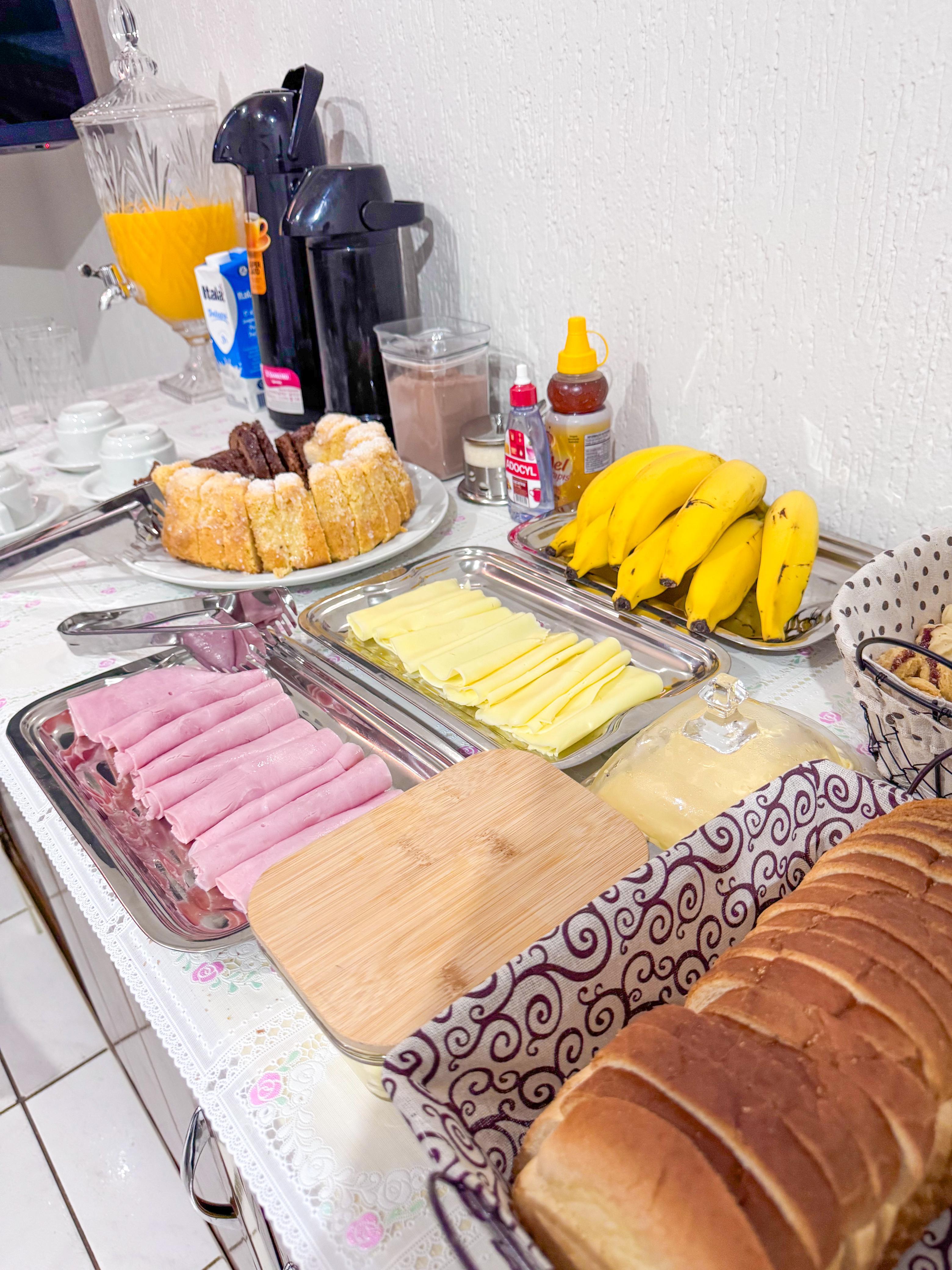 Travessas de frios, pães e suco na mesa do café da manhã