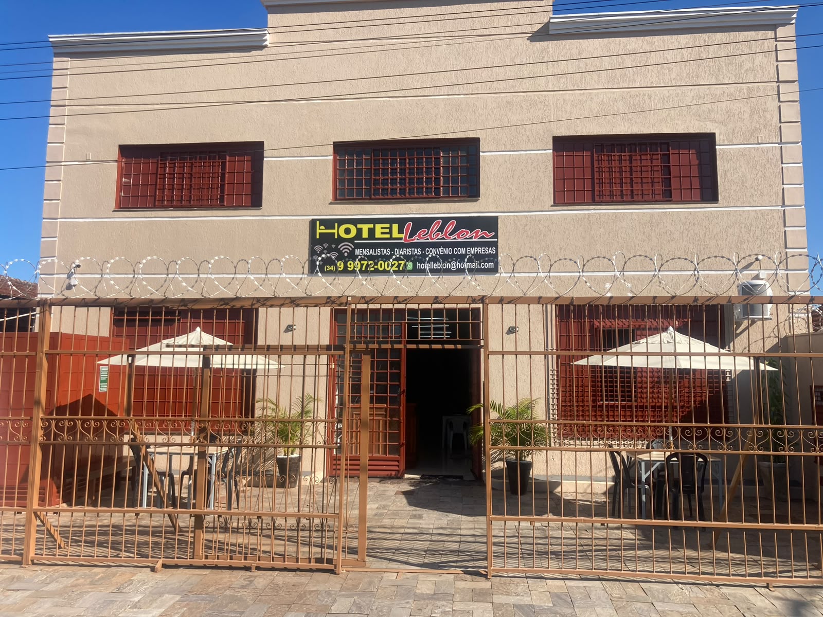 Fachada do Hotel Leblon com a placa do hotel e mesas com ombrelones na frente