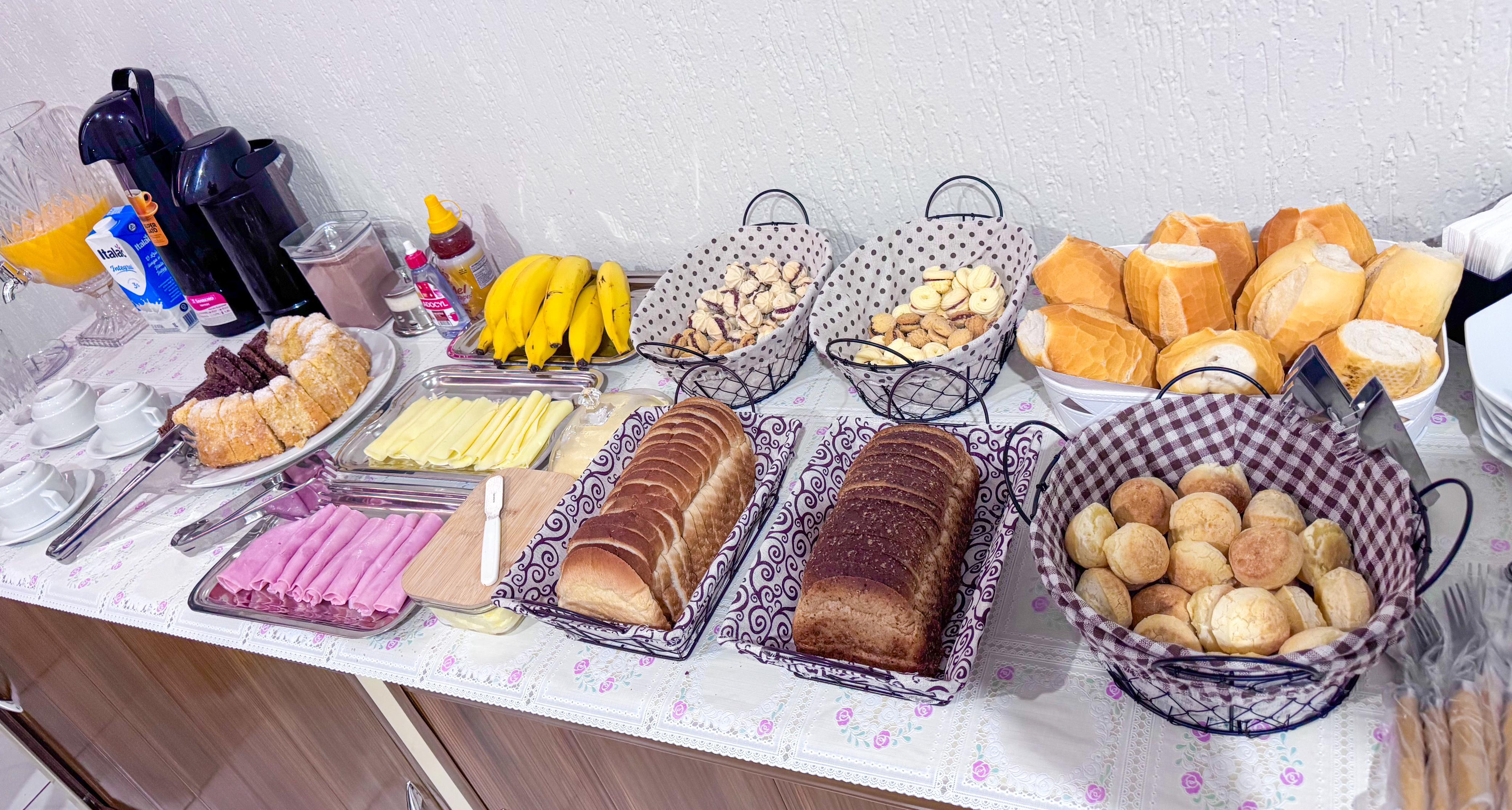 Mesa de café da manhã do hotel com pães, frios, frutas, bolo e suco