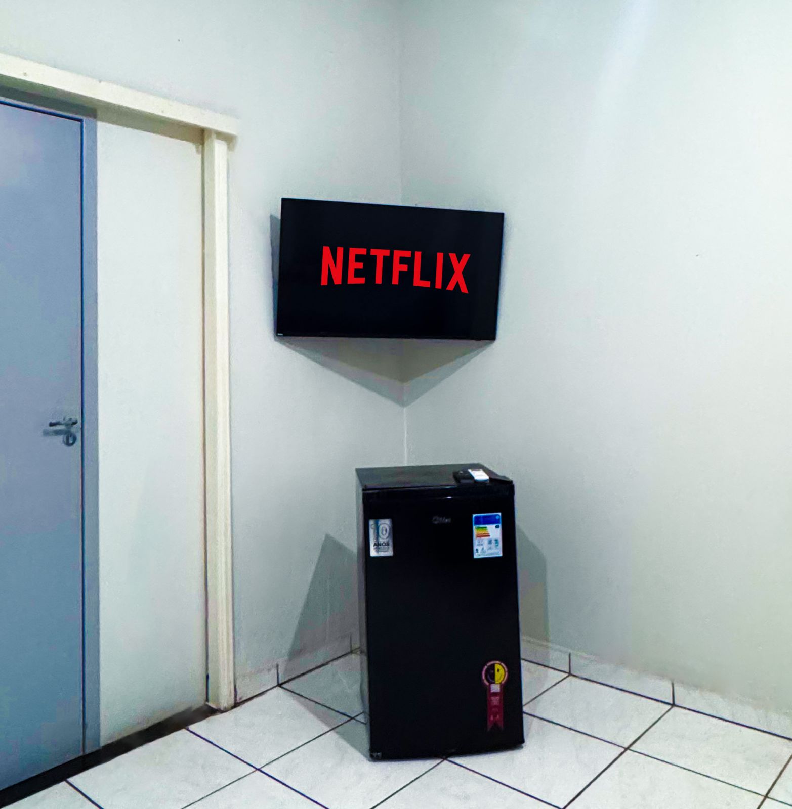 TV de parede ligada e frigobar no quarto